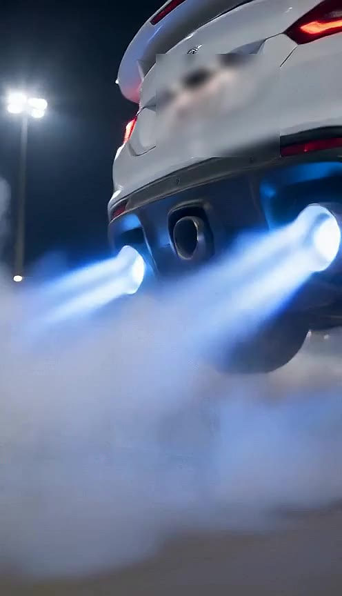 Close view of two bright blue exhaust jets firing beneath the rear bumper of a white sports car at night
